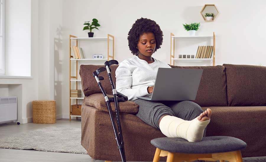 African American woman with a broken leg in cast looking for NYC personal injury lawyers on her laptop​