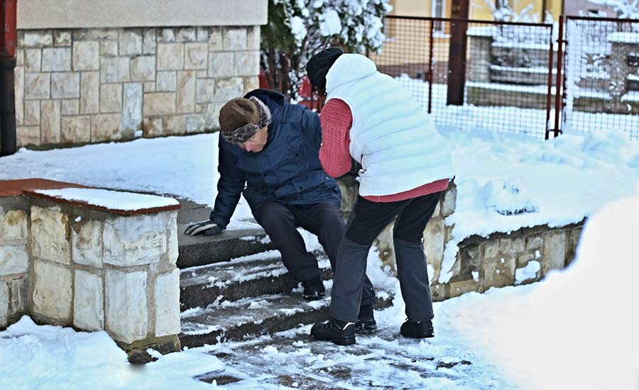 A woman trying to help a senior man who has slipped on icy stairs​