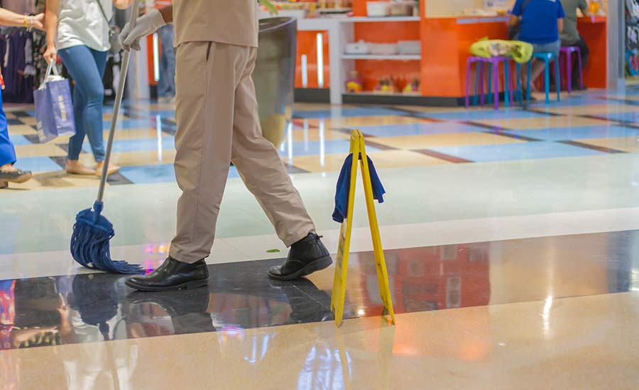 A person cleaning the floor in the mall, along with a sign "Wet floor"​
